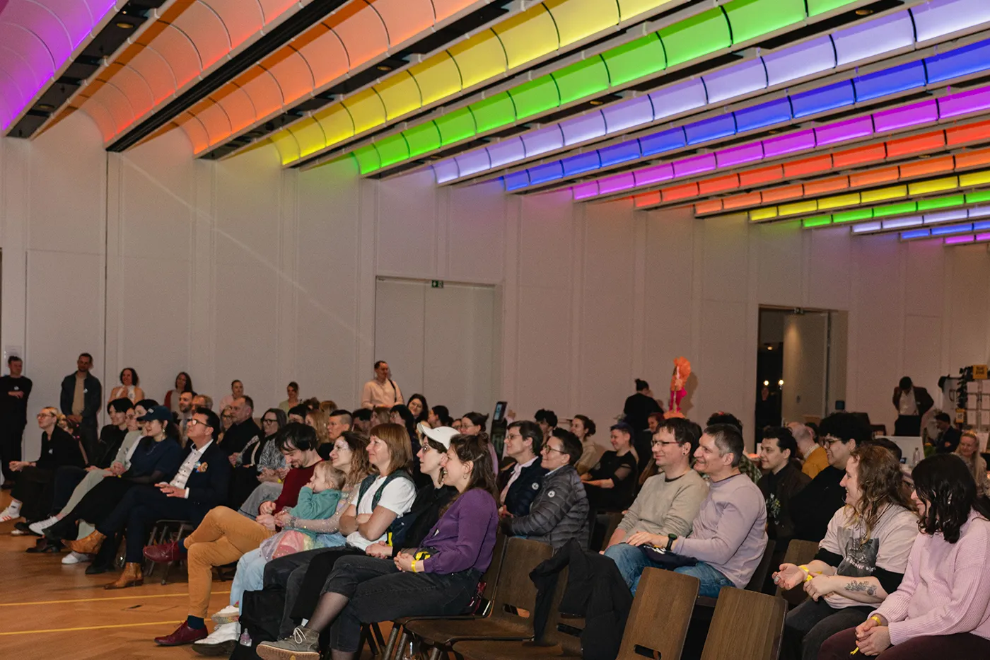 Publikum im Messesaal unter der regenbogenfarben beleuchteten Decke