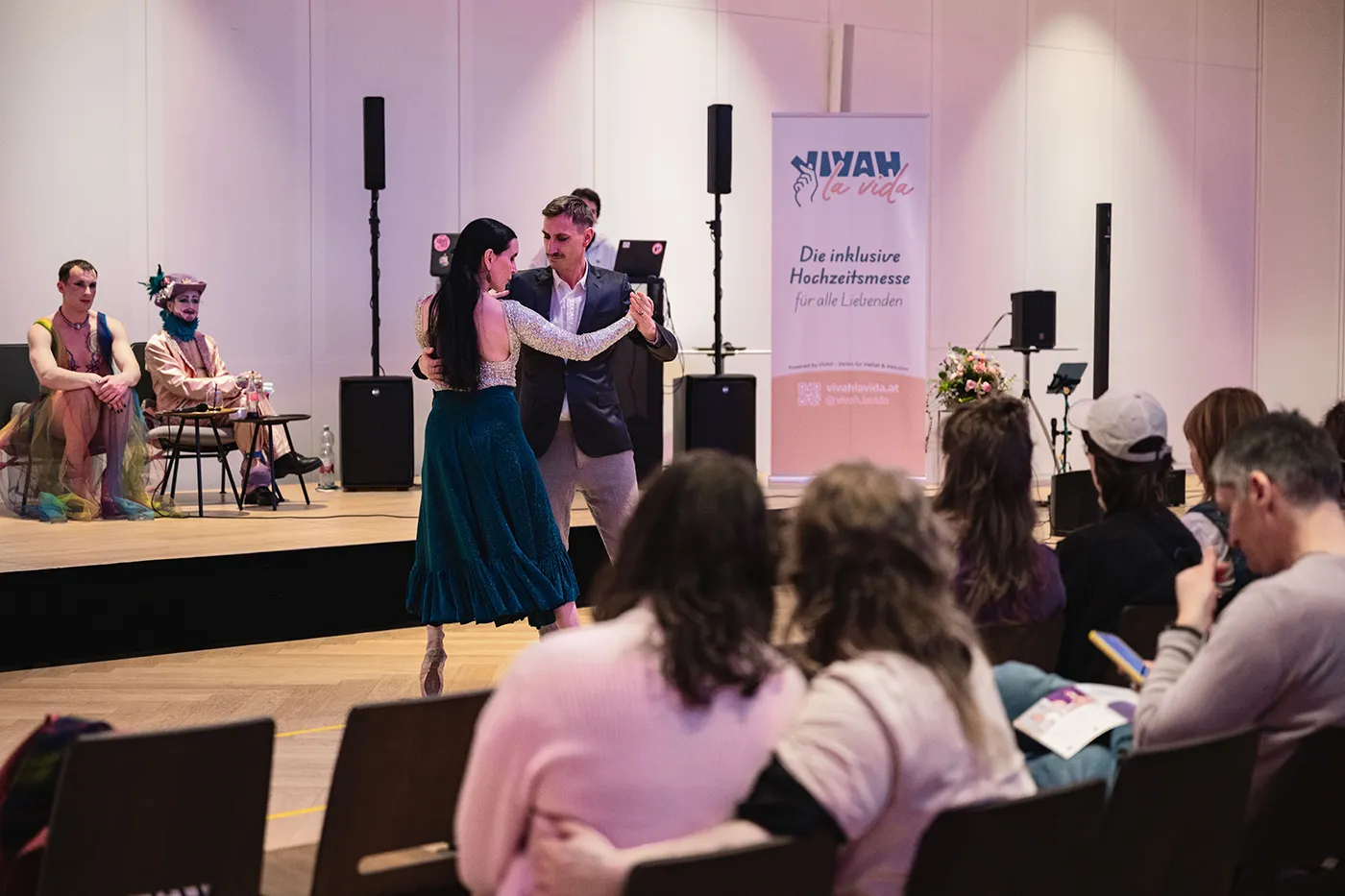 Tanzpaar auf der Bühne neben dem Vivah la Vida Rollup, davor das Publikum