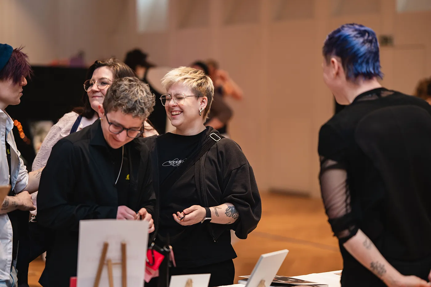 Besucher:innen lachen an einem Stand mit kleinen Kunstdrucken