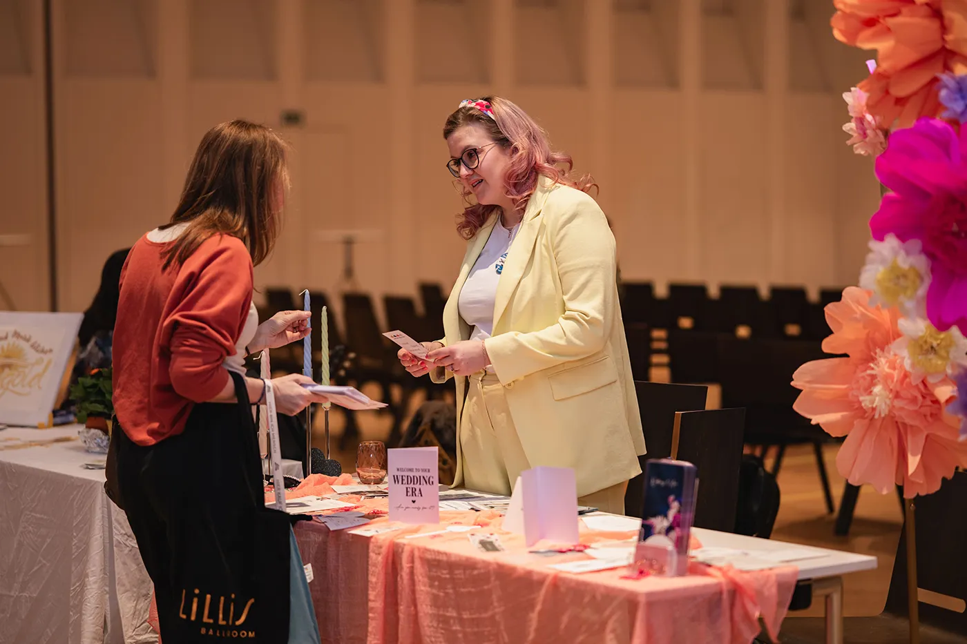 Ausstellerin berät eine Besucherin an einem pastellfarben dekorierten Stand