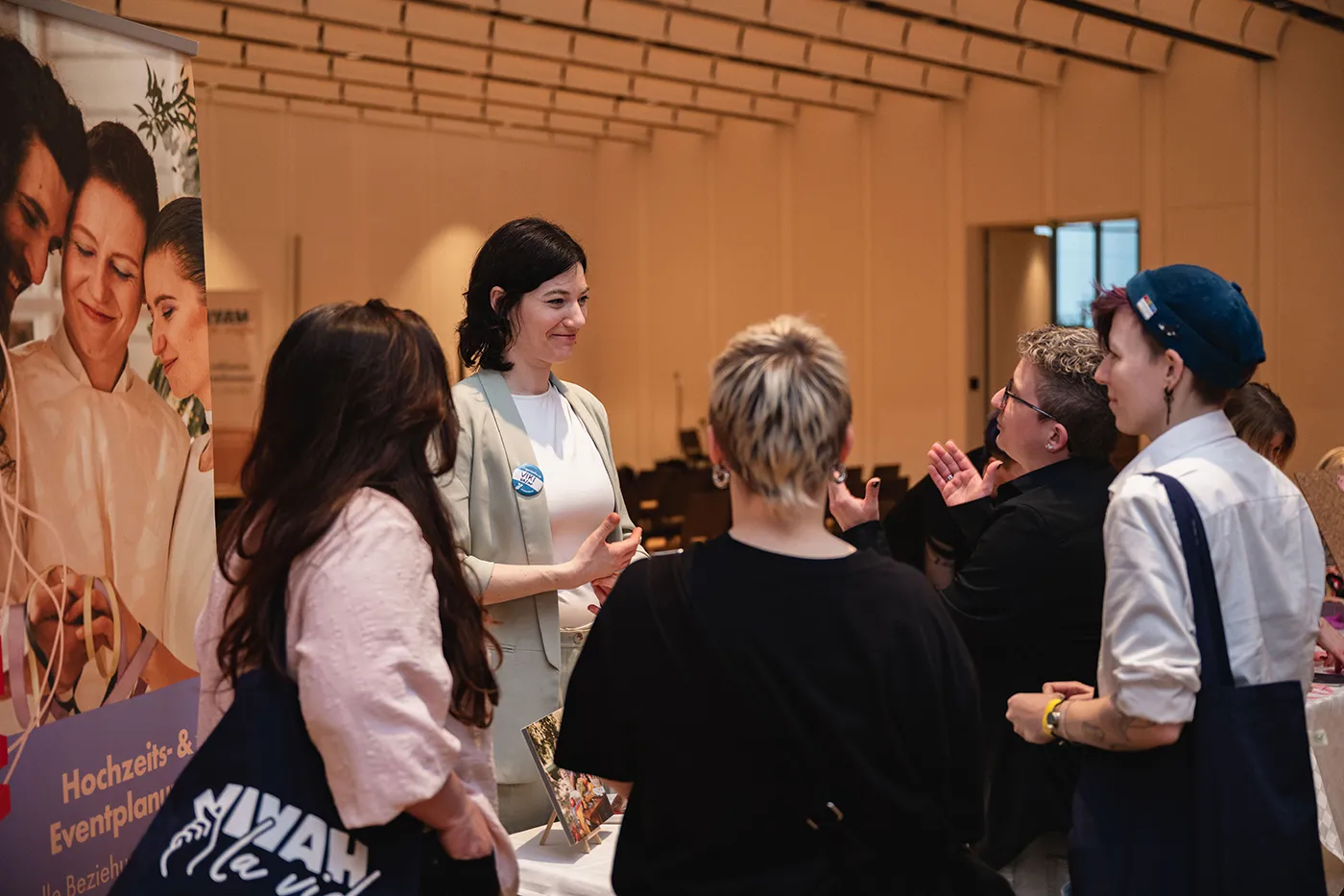 Ausstellerin im Gespräch mit Besucher:innen vor einem Rollup für Hochzeits- und Eventplanung