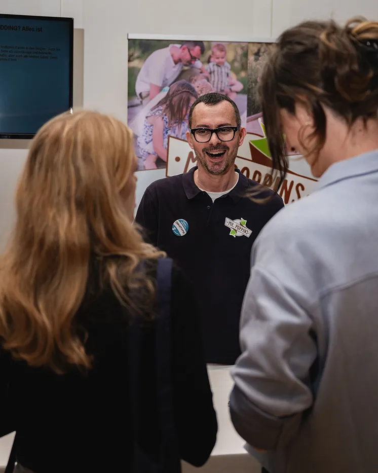 Aussteller im Gespräch mit zwei Besucherinnen an seinem Messestand