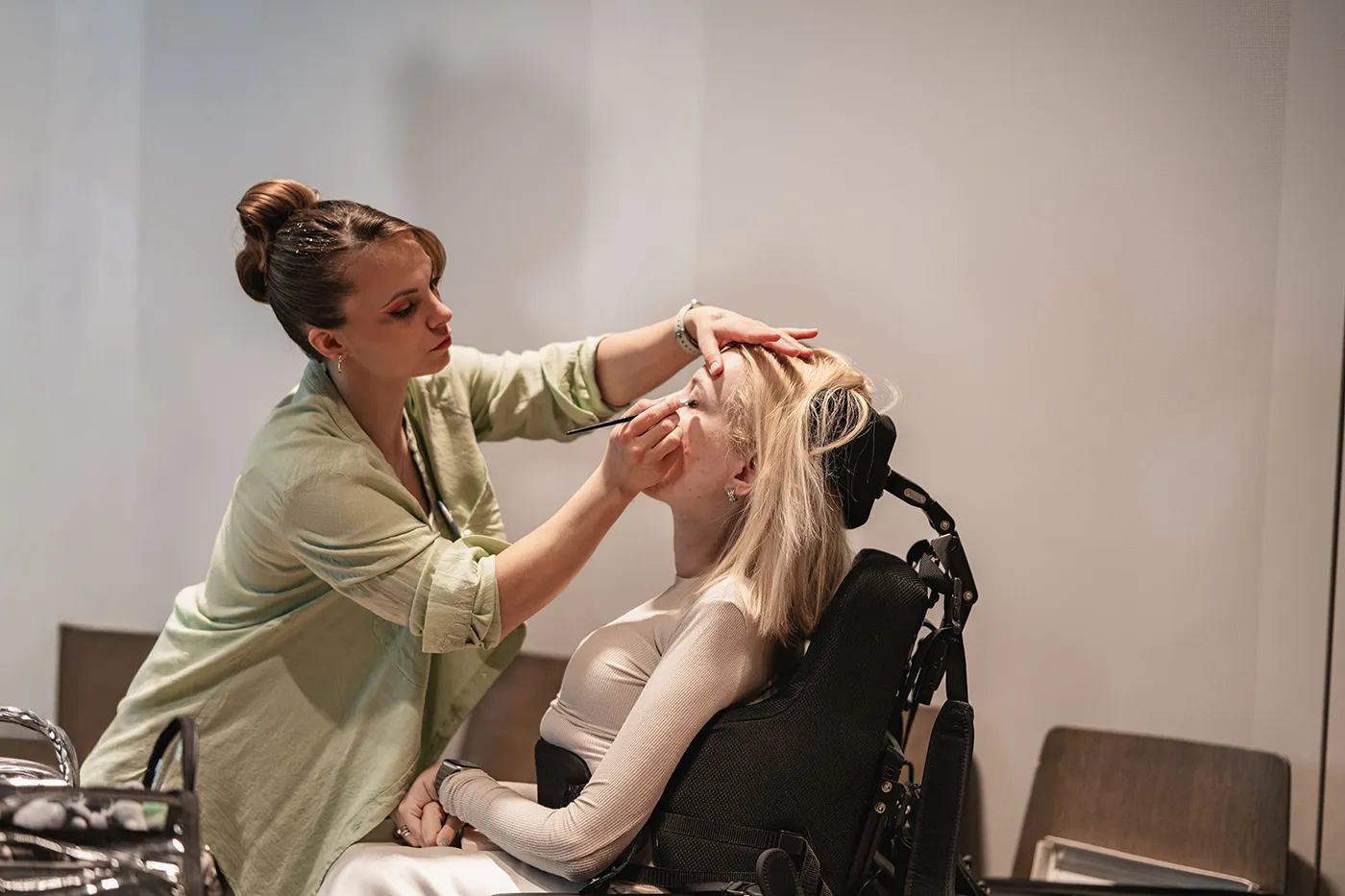 Visagistin schminkt ein Model im Rollstuhl backstage