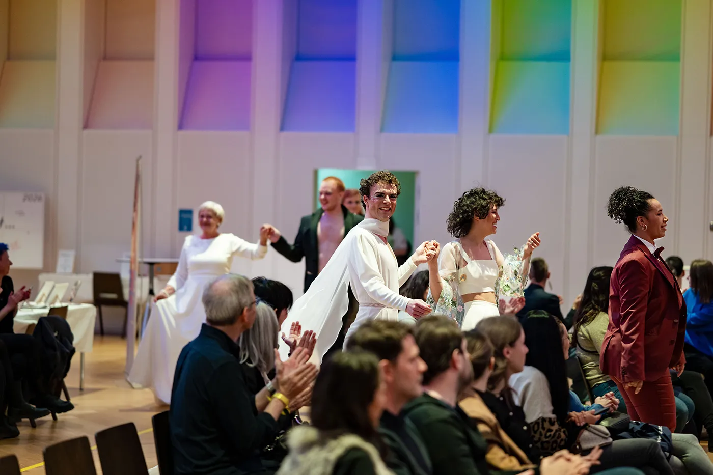 Models in Hochzeitsoutfits gehen durch den Saal, das Publikum applaudiert