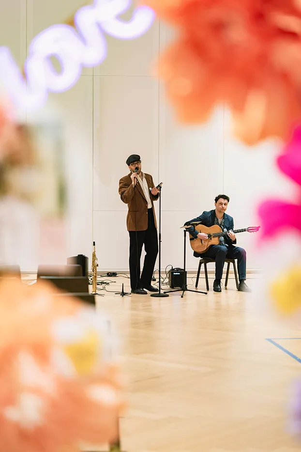 Sänger und Gitarrist beim Auftritt, umrahmt von Papierblumen