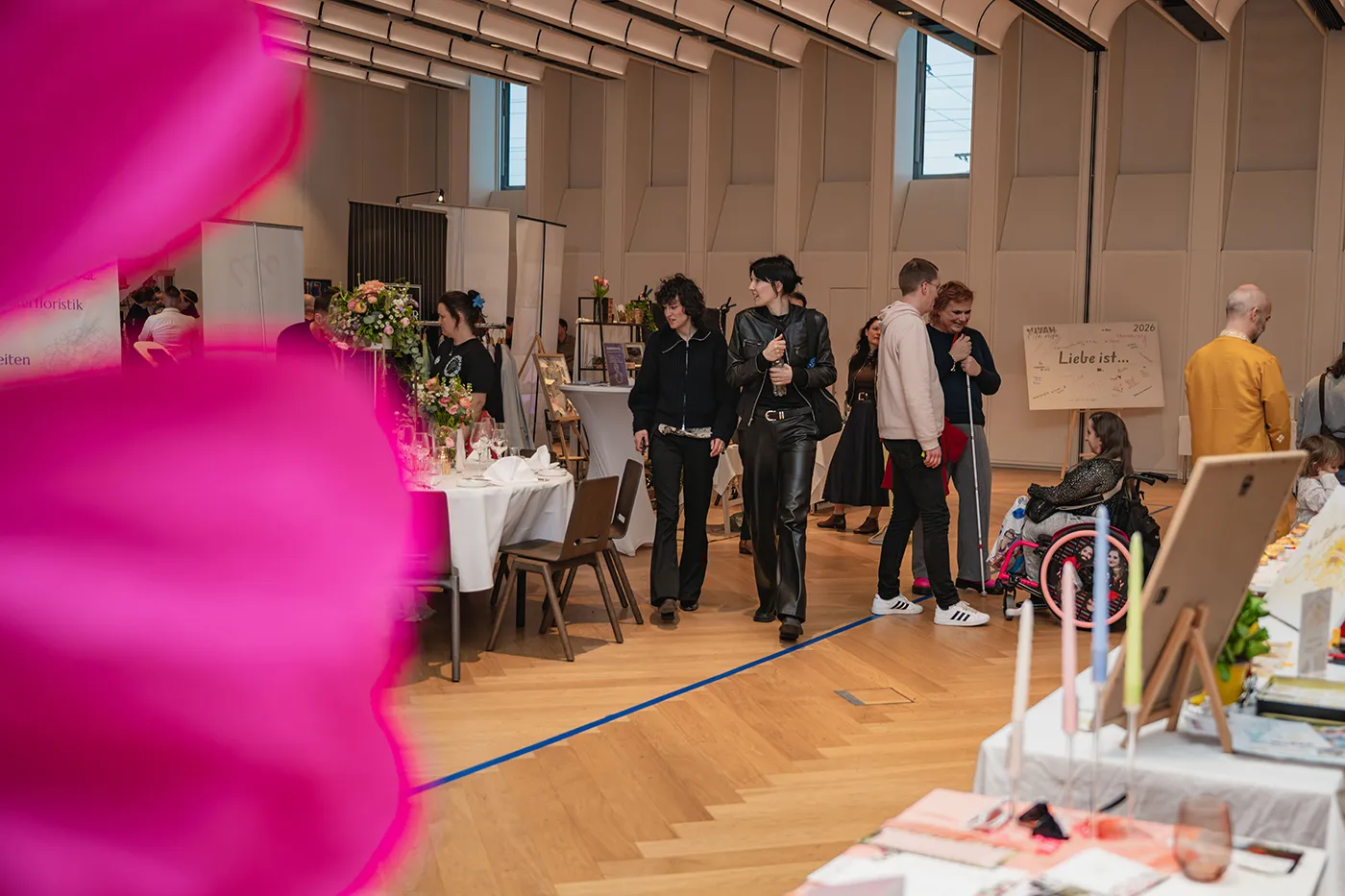 Blick durch rosa Papierblumen auf die Messestände in der Halle