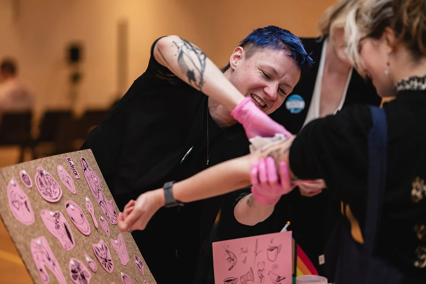 Ausstellerin trägt lachend ein Klebetattoo auf den Arm einer Besucherin auf