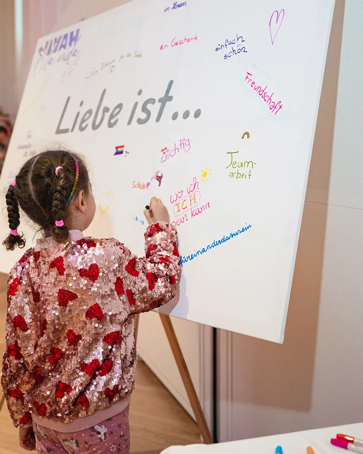 Kind schreibt auf die Mitmach-Tafel „Liebe ist …“