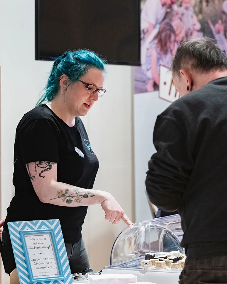 Ausstellerin bietet Besucher:innen Kostproben an ihrem Stand an