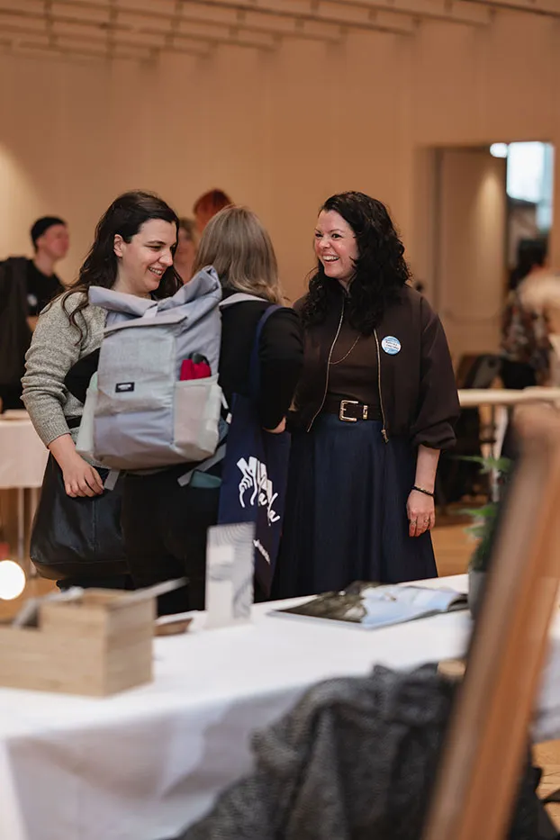 Ausstellerin und Besucherin lachen gemeinsam an einem Messestand