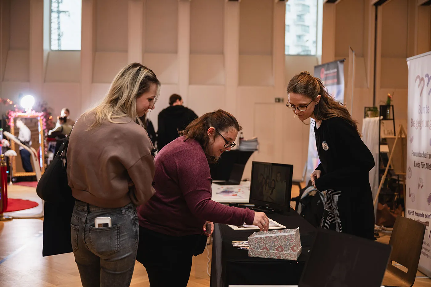 Ausstellerin zeigt zwei Besucherinnen ihre Arbeiten