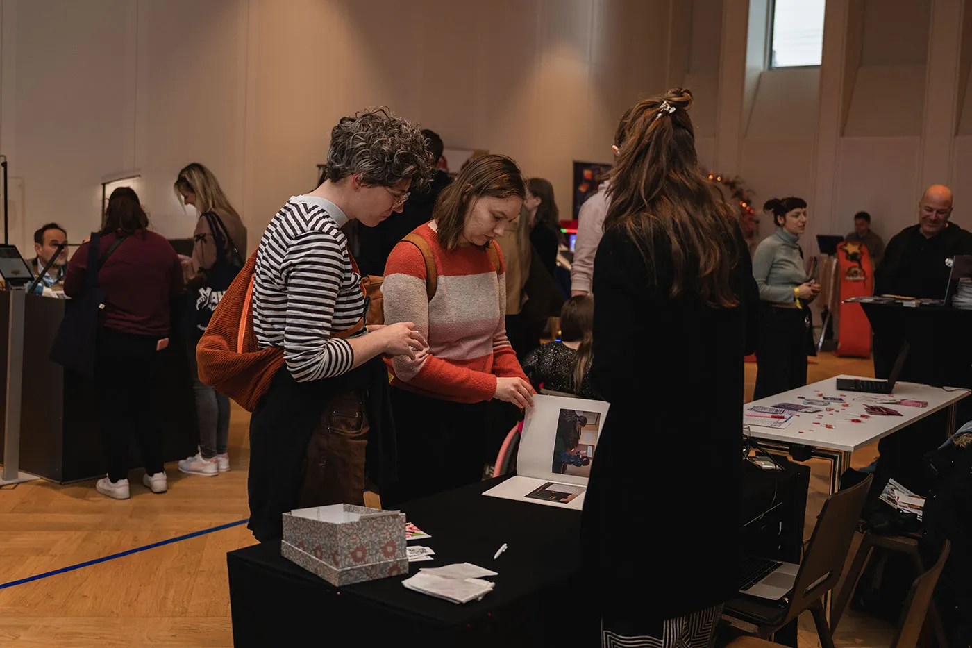 Besucherinnen sehen sich Fotoabzüge an einem Messestand an