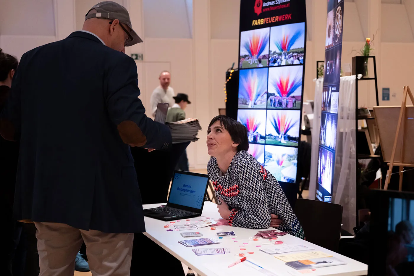 Ausstellerin berät am Stand mit Bildern von Feuerwerksshows