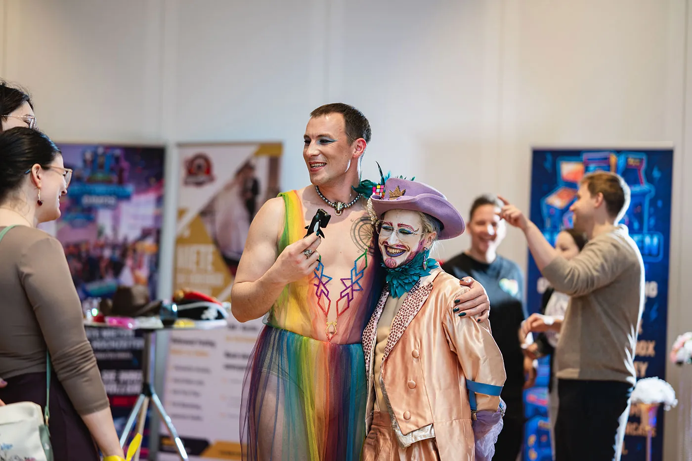 Moderierende Person im Regenbogenkleid mit Mikrofon umarmt eine Drag-Künstlerin