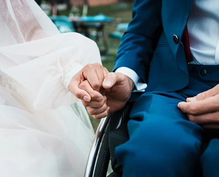 Eine Person in einem weißen Kleid und ein andere in einem blauen Anzug halten Hände